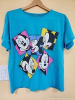 Front view of turquoise large T-shirt with five Mickey Mouse faces graphic.