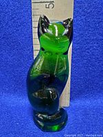 Front view of the emerald green glass cat figurine next to a ruler showing a height of approximately 3.5 inches.