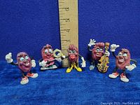Five vintage California Raisins vinyl figures posed in front of a ruler for size reference, showing approximate height around 3.5-4 inches.