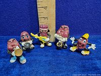 All five California Raisins vinyl figures arranged on blue felt with a ruler for size indicating approximately 2 to 3 inches tall each.