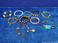Lot of 10 vintage bracelets and bangles on blue cloth background, showing various styles and colors.