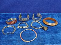 Overview of all nine bracelets and bangles on blue background, showing material variety including enamel, wood, and metal.