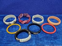 Eight vintage bracelets including white, peach, yellow, orange, black vinyl with text, and pink-purple Lucite cuff, plus black beaded bracelet