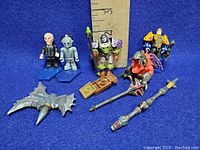 Photo of seven Lego compatible mini figures on blue bases with various weapons and accessories in front of a ruler showing about 2.5-3 inch height