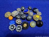 Photo showing various vintage buttons with rhinestones, metal, fabric-covered, and resin materials laid out on blue velvet background.