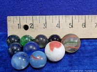Ten assorted vintage marbles arranged in front of a ruler showing size around 1 inch each.