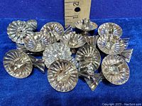 Lot of sixteen vintage metal clip-on candle holders arranged together with a ruler for size reference.