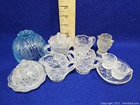 Wide shot of all miniature glass items in the lot, including lamp shade, butter dish, vase, and other cut glass pieces with ruler for size reference.
