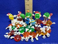 Full lot of vintage M&M's vinyl figures and cake candle holders arranged on table with ruler for scale