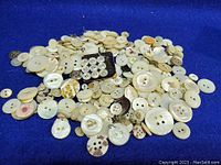 Wide view of the assorted vintage mother of pearl buttons on a blue background, showing variety and condition.