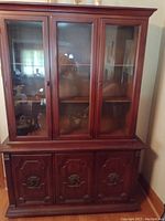 Full view of the front of the wooden china closet showing three glass doors on top section with shelves behind and three solid wood doors on the bottom with metal handles.