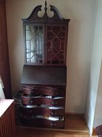 Front view of wood secretary desk showing glass doors, drop-down leaf in closed position, and four drawers.