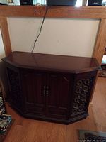 Front view of dark wooden stereo console with carved side panels, two central cabinet doors, and flat top surface.
