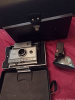 Polaroid Automatic 350 Land Camera inside original black carrying case with latch. Detachable vintage flash unit beside camera.