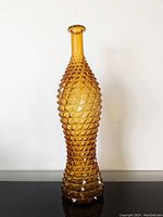 Front view of the amber hobnail glass genie bottle showing tall, textured diamond pattern and flared mouth.