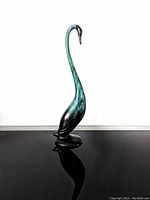 Front view of tall blue-green and black swan pottery figurine with long neck on black reflective surface against white background