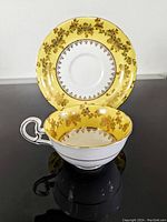 Yellow and gold filigree Royal Grafton tea cup and saucer set, showing cup inside saucer on black surface