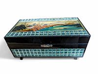Black lacquer rectangular jewelry box closed, showing Japanese landscape scene on top under glass surrounded by small greenish-blue tiles and metal clasp on front.