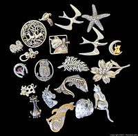 Top-down view of the 20 silver toned vintage figural brooches on black background, showing various animal, floral and fantasy designs.