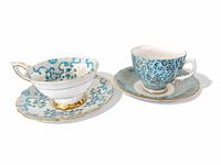 Two blue bone china tea cups and saucers are placed side by side, showing the overall design, shape, and pattern colors: one white with blue flowers, one light blue with black floral patterns.