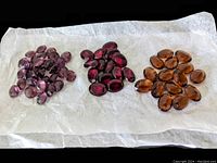 Three groups of faceted Czech glass crystal cabochons in amethyst, ruby red, and smoky topaz colors laid on white tissue paper.