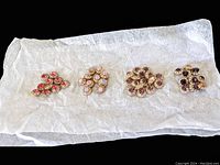 Four gold-tone crystal components in various pink and red shades laid out on tissue paper, showing size and color variations.