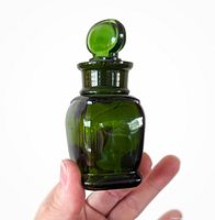 Photo showing the emerald green apothecary bottle held in hand to illustrate size and details of the glass stopper and bottle body.