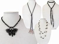 Four vintage black bead necklaces displayed on busts including Miriam Haskell butterfly necklace and long bead necklaces.