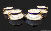 Four cobalt blue and gold gilt porcelain teacups and matching saucers shown on black background, arranged in two pairs.