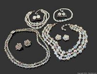 Full lot image showing 4 necklaces and 4 pairs of clip-on earrings arranged on black cloth surface, highlighting bead clarity and vintage style.