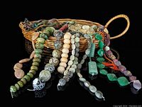 Woven basket containing strands of assorted semi-precious gemstone beads and silk tassels draped over it.