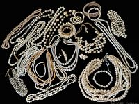 Overall view of large assortment of vintage faux pearl necklaces, bracelets, earrings, and hair pins arranged on white surface. Various styles and sizes visible from single strands to multi-strand pieces.