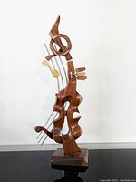 Front view of abstract hand-carved wooden and metal violin sculpture showing musical notes and organic shapes.