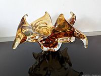 Front-side view of amber-tone Chalet glass bowl showing curved points and organic shape on black reflective surface.