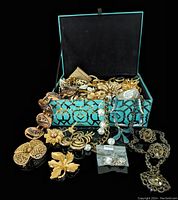 Open turquoise mirrored glass jewelry box filled with assorted vintage costume jewelry pieces including brooches and chains