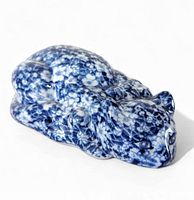 Side view of blue and white floral ceramic sleeping cat figurine showing intricate floral pattern and curled up resting pose.