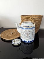 Ceramic teapot with intricate blue and gold patterns and bamboo-style handle next to the woven basket and lid