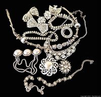 Photo showing multiple rhinestone jewelry pieces including necklaces, brooches, and bracelets arranged on a black background highlighting their silver-tone base and clear rhinestones with some large pearl-like beads.