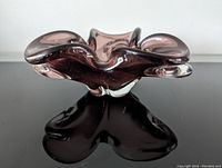 Front view of the purple amethyst Murano glass bowl placed on a reflective black surface showing the organic wavy design and transparency of the glass.
