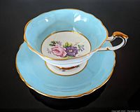 Tea cup resting inside matching saucer showing robin's egg blue color, scalloped edges, floral interior design, and gold trim.