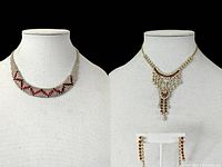 Two necklaces and a pair of earrings displayed on white busts and stand against black background. Left necklace is silver-tone with red zigzag pattern in clear rhinestones. Center is gold-tone bib necklace with cascading clear and red rhinestones. Earrings are drop style with red and clear rhinestones