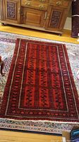 Full view of the red Persian style area rug with geometric patterns and fringe laid flat on a floral patterned larger rug, showing overall condition and color.