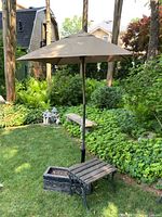 Outdoor photo showing entire set: wooden slat bench with wrought iron legs, planter box, umbrella stand with beige umbrella open.