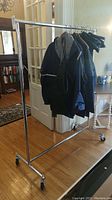Full view of the chrome clothing rack holding some clothes, showing general structure and size in room setting.