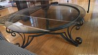 Wide angle image showing the entire round glass top coffee table and the wrought iron scrollwork base.