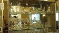 Two glass shelves filled with various glassware items including decanters, pitchers, and stemmed glasses.
