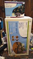 Two boxed items: Aquascape Pond and Landscape Light Kit (blue and white box) and Aquascape Crazy Legs Frog Spitter water feature (white box) stacked together.