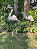 Pair of metal bird sculptures standing in a garden, showing overall size and design.
