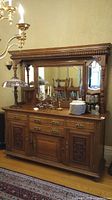 Full front view of the wooden sideboard with mirror hutch, holding various tableware items and lamps, showing detailed brass pulls and carved woodwork.