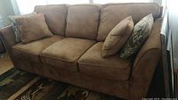 Front-right angle of caramel ultrasuede sofa with three seat cushions and throw pillows.